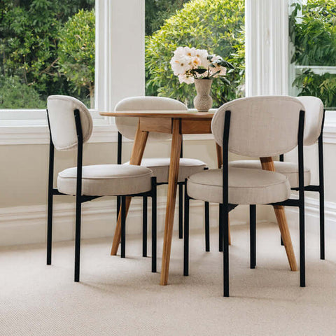 Dining area with a wooden table and four chairs in a bright room with large windows.