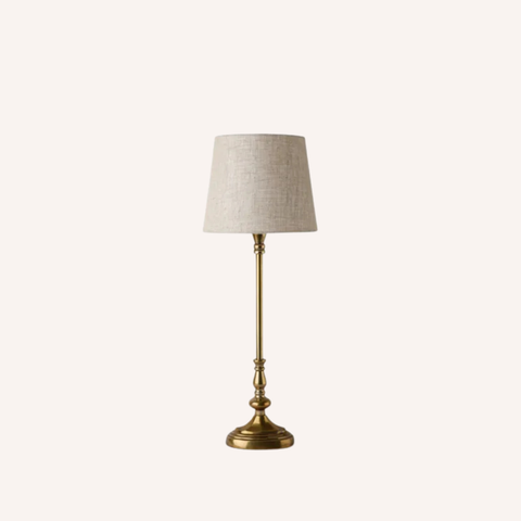 A classic table lamp with a textured beige linen drum shade and a polished brass-finished metal base, shown against a solid off-white background.