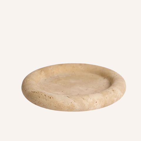 A round travertine stone tray with a natural textured surface, shown on a solid off-white background.
