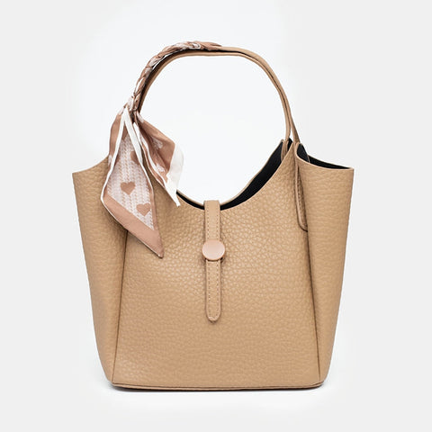 A structured beige pebbled leather handbag with a top handle, a decorative light pink scarf tied to the handle, and a central strap closure, shown against a plain white background.