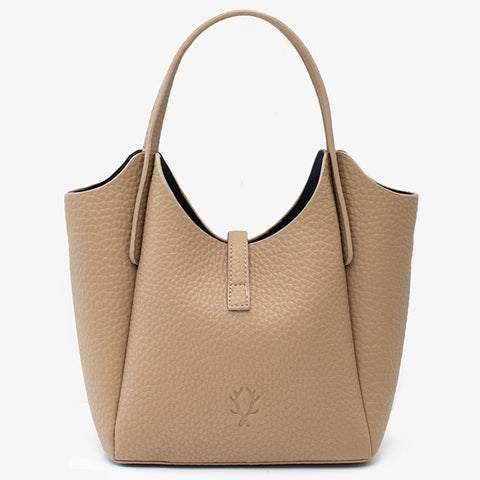 A structured pebbled leather handbag in a light tan/beige color, featuring dual top handles, a small central tab, and a debossed lotus flower logo on the front, set against a plain white background.