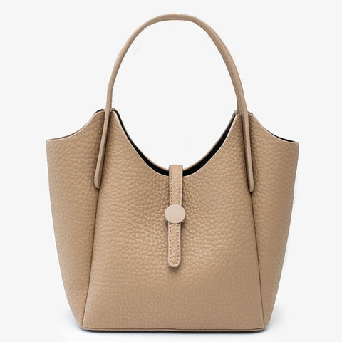 A structured pebbled leather handbag in a light tan/beige color, featuring dual top handles and a central strap closure with a round button, set against a plain white background.
