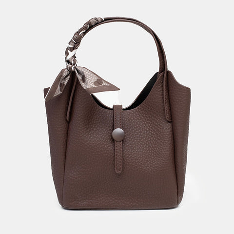 A dark brown pebbled leather handbag with a top handle, a decorative bow detail on the strap, and a silver snap button closure on the front flap, shown against a plain light gray background.