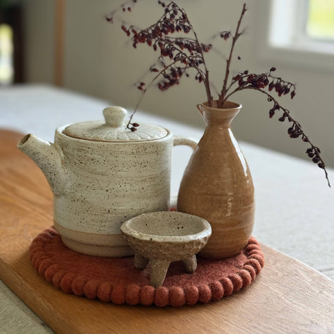 Ceramic teapot, small bowl, and vase on a wooden surface with a blurred indoor background