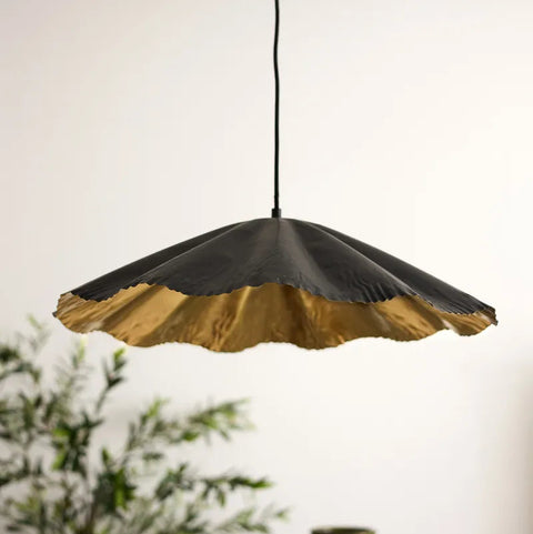 Black and gold pendant light with a blurred plant and vase in the background