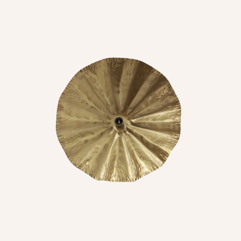 A round, gold-toned decorative pendant light with a textured, fan-like radial pattern and a small black center, shown against a solid off-white background.