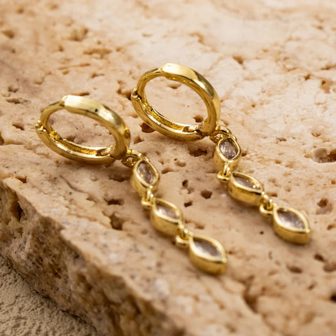 Marquise Triple Drop gold huggie earrings with clear zirconia drops on a textured beige surface