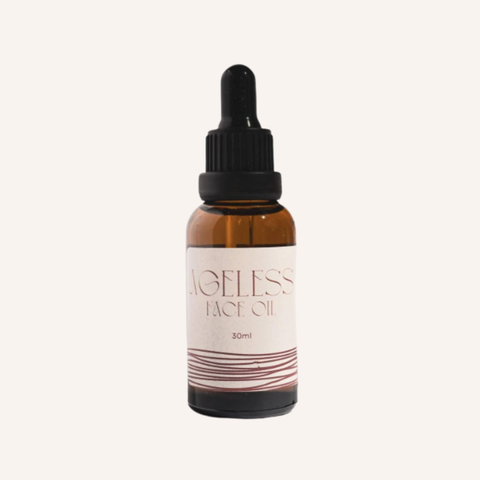 An amber glass dropper bottle of Ageless Face Oil with a black dropper cap and a cream-colored label, centered on a light beige background.