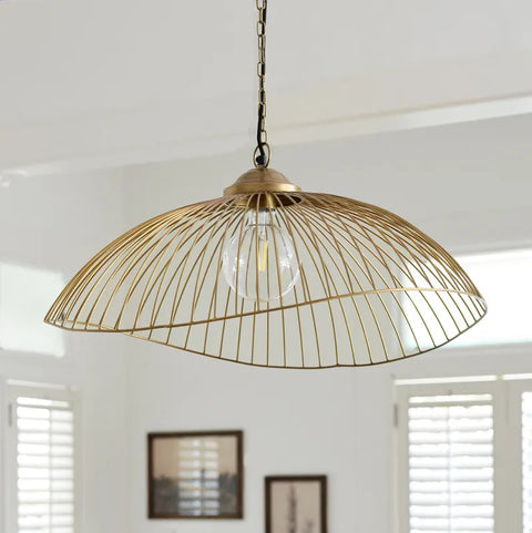 A brass wire cage pendant light hanging from a chain in a bright, modern room with white walls and window shutters.