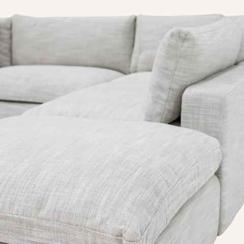 Close-up of a light gray textured fabric sectional sofa with plush cushions and a chaise lounge.