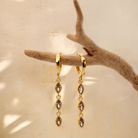 Marquise Triple Drop gold huggie earrings hanging from a driftwood branch
