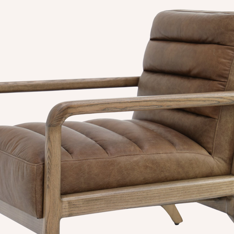 A close-up of a modern armchair featuring a tufted brown leather seat and backrest with a light natural wood frame and armrests, set against a plain off-white background.