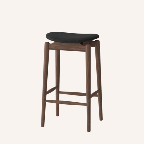 A modern bar stool with a dark charcoal gray upholstered seat and a medium brown wooden frame with four legs and front support bars, shown against a solid off-white background.