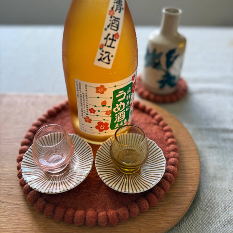 Bottle of Japanese sake with two glasses on a wooden tray and felt trivet