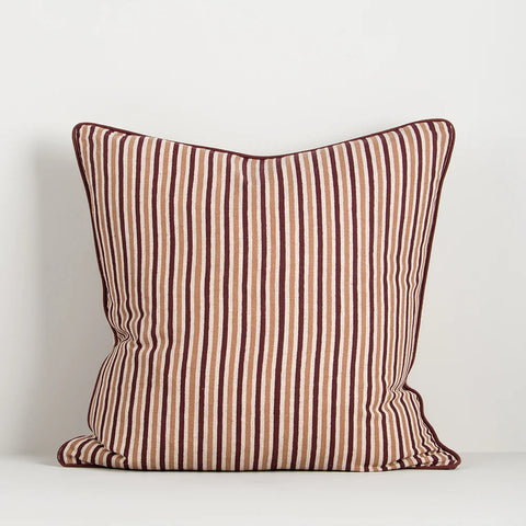 A square throw pillow with vertical stripes in brown, rust red, and cream, featuring a matching piped edge, set against a plain light gray background.