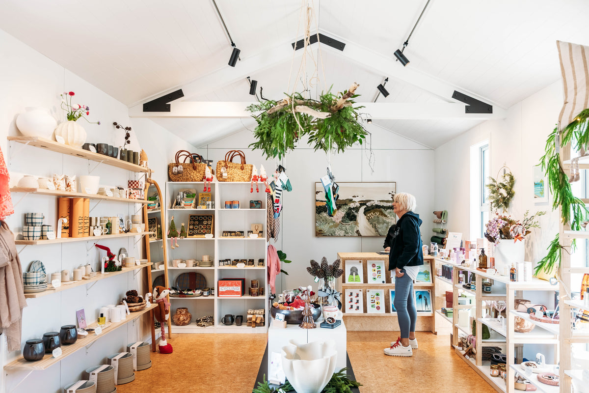 Inside Shop Curated at Luggate Village: homewares, gifts and seasonal pieces on timber shelving beneath a hanging greenery installation