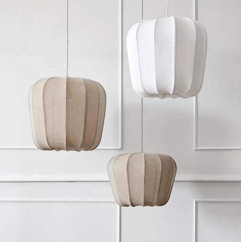 Three modern pleated pendant lights in white and beige fabric, hanging against a white paneled wall.