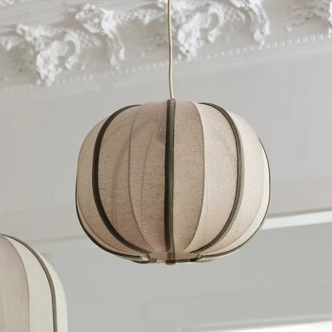 Round beige pendant light hanging against a decorative white wall.