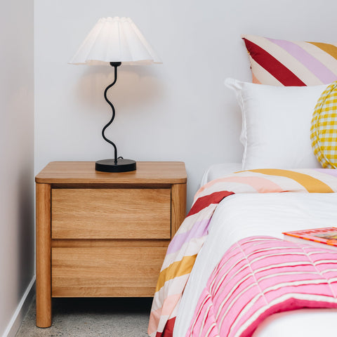 Bedroom with wooden nightstand, lamp, and colorful bedding.