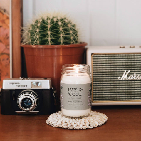 Candle labeled 'Ivy & Wood' on a table with a camera and radio in the background