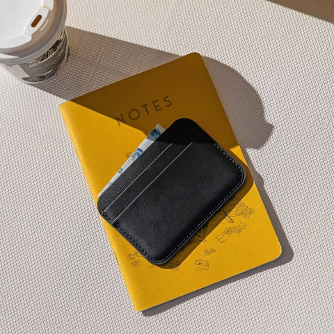 Black cardholder on a yellow notebook with a coffee cup in the corner