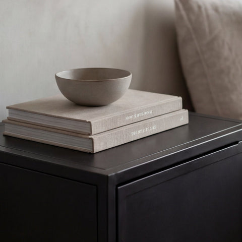 Stack of books with a bowl on top on a dark surface, with a neutral background
