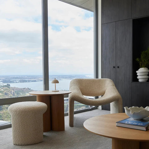 Modern living room with a large window view, beige armchair, and wooden coffee table.